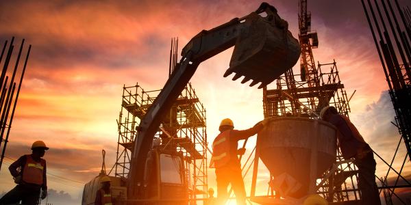 a silhouette of a construction site at sunset showing a digger, some scaffolding, and a couple of workers. 