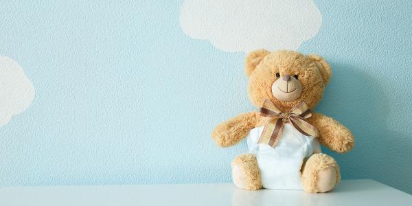 a teddy bear wearing a nappy against a pale blue painted wall with images of white clouds painted on. 