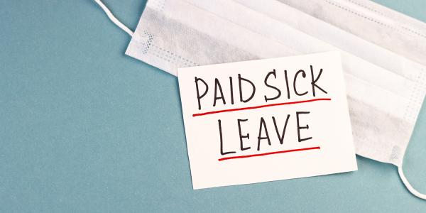 a face mask and piece of white paper with the words 'PAID SICK LEAVE' written on it against a blue background. a face mask and piece of white paper with the words 'PAID SICK LEAVE' written on it against a blue background.