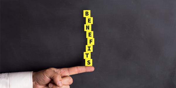 a person balancing yellow blocks on their finger, the blocks each have a letter written on them together spelling the word 'BENEFITS'