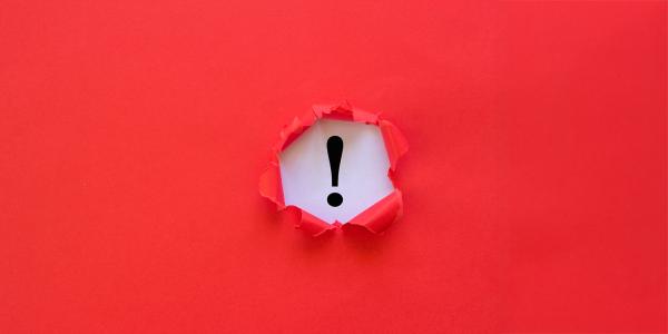 a red sheet of paper with a hold in the middle, underneath is a white sheet of paper with a thick black exclamation mark on it. a red sheet of paper with a hold in the middle, underneath is a white sheet of paper with a thick black exclamation mark on it.