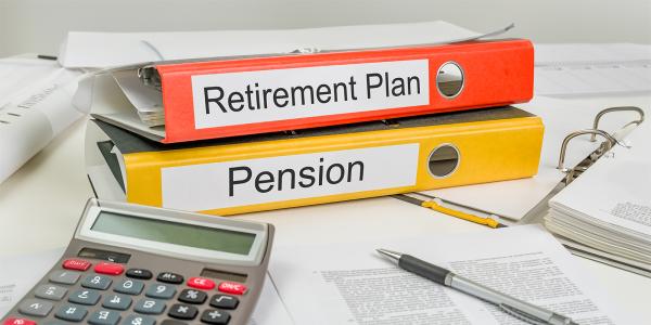 a desk with scattered paperwork, a calculator and 2 folders, written on the spines of the folders are the words 'PENSION' and 'RETIREMENT PLAN' a desk with scattered paperwork, a calculator and 2 folders, written on the spines of the folders are the words 'PENSION' and 'RETIREMENT PLAN'
