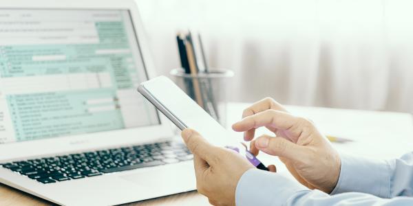 person holding a mobile phone whist using a laptop