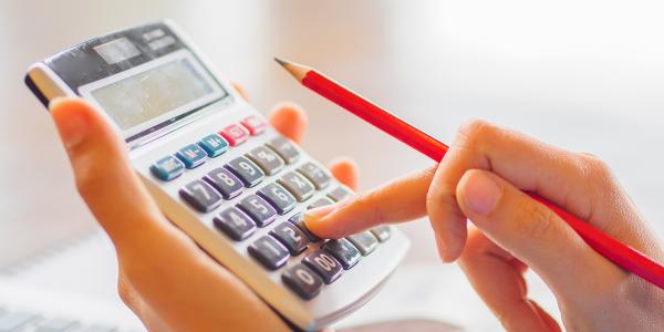 person typing on a calculator whilst holding a pencil