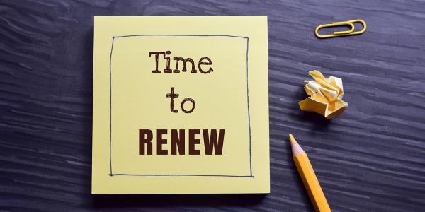 a wooden desk, on top sits a yellow pencil, a yellow paperclip, a screwed up post-it note and a post-it note with the words 'TIME TO RENEW'