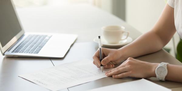 a person sat at a desk with a laptop, signing a document. 