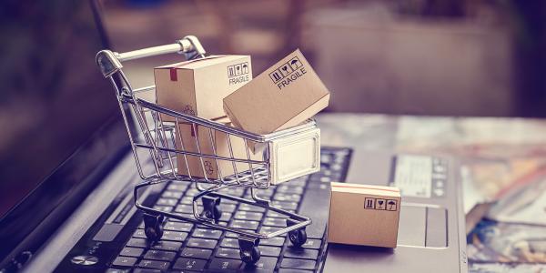 an open laptop with a tiny shopping trolley sat on the keyboard, inside the trolley are tiny brown parcels. an open laptop with a tiny shopping trolley sat on the keyboard, inside the trolley are tiny brown parcels.