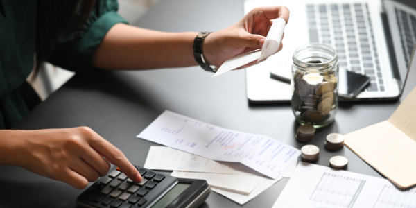 A person sat at a desk, adding up receipts on a calculator. 