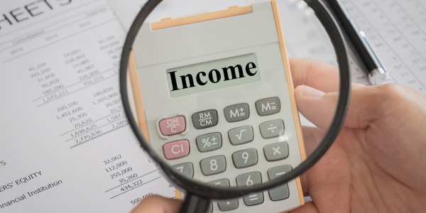 a person holding a magnifying glass up to a calculator showing the word 'INCOME' on the screen, behind this paperwork can be seen. a person holding a magnifying glass up to a calculator showing the word 'INCOME' on the screen, behind this paperwork can be seen.