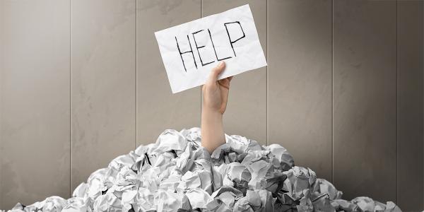 a mound of crumpled up papers with an arm sticking out holding a sheet of paper with the word 'HELP' written on it. 