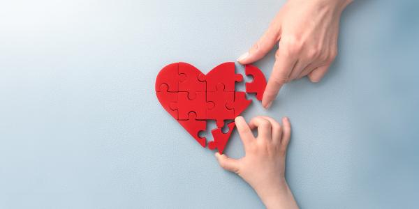 2 people completing a jigsaw puzzle, the puzzle is a red heart