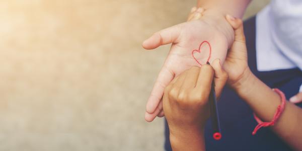 a child drawing a love heart on an adults palm with red pen.