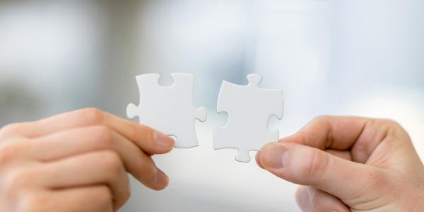 2 people each holding a jigsaw piece, the pieces look as if they fit together 