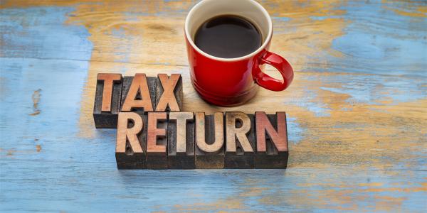 wooden letters arranged on a desk to spell 'TAX RETURN' next to this is a red cup of coffee. 