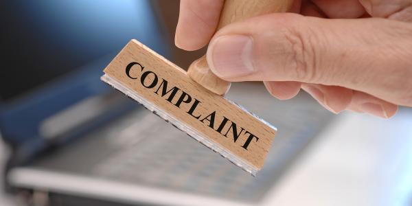 a person holding a wooden stamper, the stamper is for the word 'COMPLAINT' 