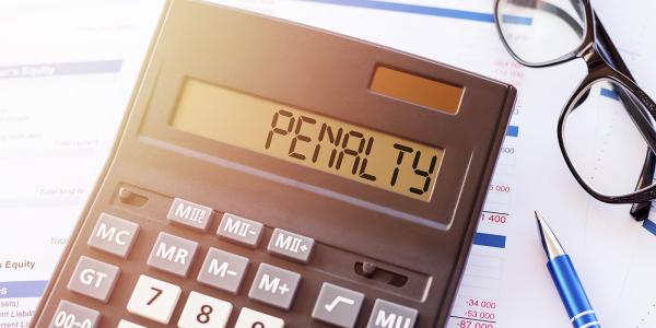 a calculator with the word 'PENALTY' typed on it. next to the calculator a pair of glasses and a pen can be seen. the background is paperwork. 