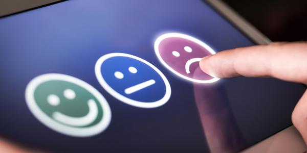 tablet showing 3 faces, a happy face, a indifferent face, and a sad face to rate service. A person is pressing the sad face tablet showing 3 faces, a happy face, a indifferent face, and a sad face to rate service. A person is pressing the sad face
