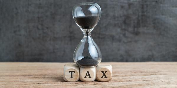 An hour-glass emptying, sitting on top of the letters T-A-X An hour-glass emptying, sitting on top of the letters T-A-X