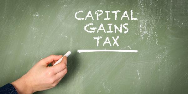 a green coloured chalkboard with a person writing the words 'CAPITAL GAINS TAX' in white chalk a green coloured chalkboard with a person writing the words 'CAPITAL GAINS TAX' in white chalk