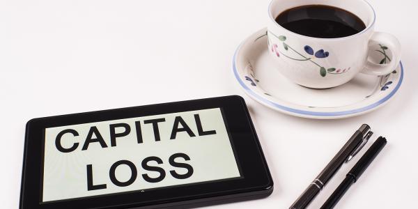 a tablet with the words 'CAPITAL LOSS' typed on the screen, two pens and a cup of black coffee. a tablet with the words 'CAPITAL LOSS' typed on the screen, two pens and a cup of black coffee.