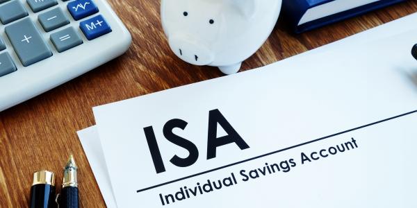 a desk with a calculator, a piggy bank, pens, a calculator and a sheet of white paper with the words 'ISA INDIVIDUAL SAVINGS ACCOUNT' written on it.