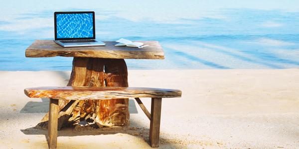a wooden desk and seat set up looking over the sea abroad, on the desk sits a laptop. a wooden desk and seat set up looking over the sea abroad, on the desk sits a laptop.