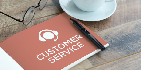 a booklet titled 'CUSTOMER SERVICE' on a desk besides a pair of glasses and a cup of tea. a booklet titled 'CUSTOMER SERVICE' on a desk besides a pair of glasses and a cup of tea.