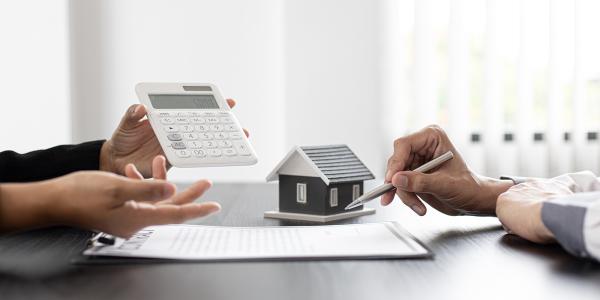 2 people sat at a desk with a contract and a model house in front of them. 2 people sat at a desk with a contract and a model house in front of them.
