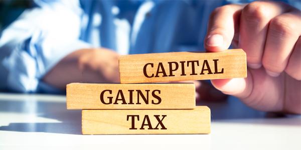 a person stacking wooden blocks, each block has a word written on it spelling out 'CAPITAL GAINS TAX' a person stacking wooden blocks, each block has a word written on it spelling out 'CAPITAL GAINS TAX'