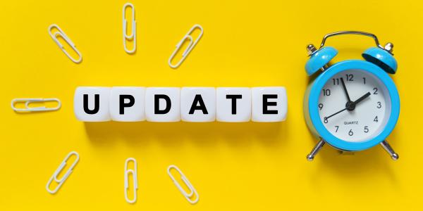 yellow background with a blue clock, the word updated written on white blocks surrounded by paperclips yellow background with a blue clock, the word updated written on white blocks surrounded by paperclips