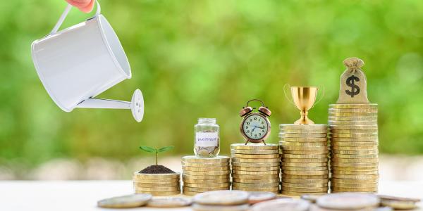 5 stacks of coins increasing in size, all have a different figure on top, from left to right: a plant growing from a pile of dirt, a person is watering the plant, a jar of coins, a clock, a trophy, a bag of money. 5 stacks of coins increasing in size, all have a different figure on top, from left to right: a plant growing from a pile of dirt, a person is watering the plant, a jar of coins, a clock, a trophy, a bag of money.