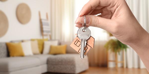 a person holding up a set of keys, the background shows a living room a person holding up a set of keys, the background shows a living room
