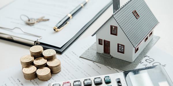 a miniature house, stacks of coins, keys and paperwork sat on a desk. a miniature house, stacks of coins, keys and paperwork sat on a desk.