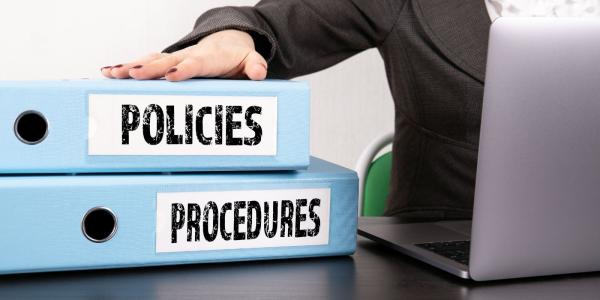 Two folders on a desk, one says 'POLICIES' and the other says 'PROCEDURES' on the side of the folders. Two folders on a desk, one says 'POLICIES' and the other says 'PROCEDURES' on the side of the folders.