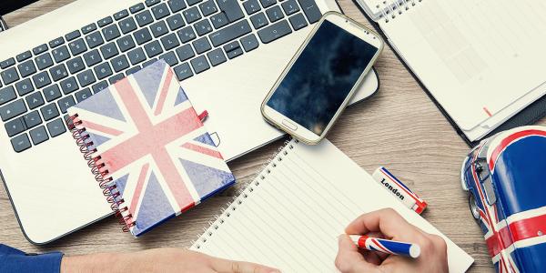 a person at a desk with a laptop, phone, notebook and various stationary with the UK flag on it a person at a desk with a laptop, phone, notebook and various stationary with the UK flag on it