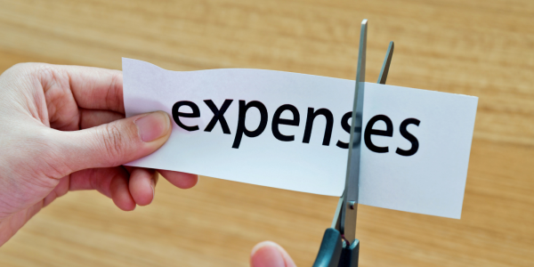 The word "expenses" typed on a piece of white paper, with scissors cutting the letters "e" and "s" at the end of the word. The word "expenses" typed on a piece of white paper, with scissors cutting the letters "e" and "s" at the end of the word.