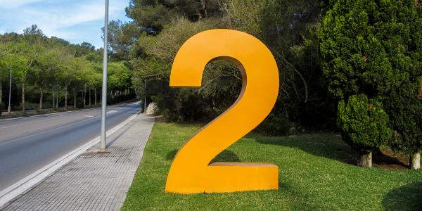 Background of a blue shy and green grass and trees next to a road. On the grass sits a large orange number 2. Background of a blue shy and green grass and trees next to a road. On the grass sits a large orange number 2.