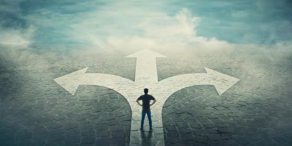 A person stood on an arrow that forks off left, right and straight ahead. A person stood on an arrow that forks off left, right and straight ahead.