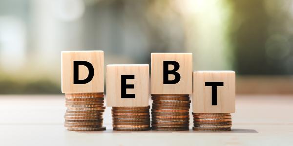 4 small stacks of coins with a wooden block on top of each one, together the blocks spell out the word 'DEBT'. 4 small stacks of coins with a wooden block on top of each one, together the blocks spell out the word 'DEBT'.