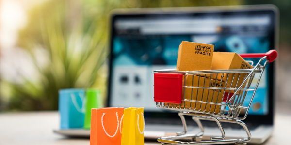 various different coloured shopping bags, a shopping trolley full of cardboard boxes and a laptop screen in the background. various different coloured shopping bags, a shopping trolley full of cardboard boxes and a laptop screen in the background.