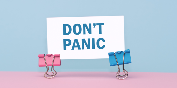 a piece of white paper with the words 'DON'T PANIC' printed in blue text, the paper is held up by 2 coloured foldback paper grips against a pink and blue background. a piece of white paper with the words 'DON'T PANIC' printed in blue text, the paper is held up by 2 coloured foldback paper grips against a pink and blue background.