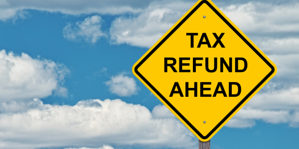 A blue sky with a yellow traffic sign with the words 'TAX REFUND AHEAD' in black text. A blue sky with a yellow traffic sign with the words 'TAX REFUND AHEAD' in black text.