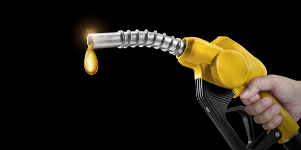 A person holding a fuel pump nozzle, the end of the nozzle is dripping with liquid gold. A person holding a fuel pump nozzle, the end of the nozzle is dripping with liquid gold.
