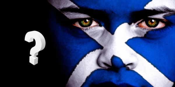 A person with their face painted as the Scottish flag against a black background, in the background a white question mark can be seen. A person with their face painted as the Scottish flag against a black background, in the background a white question mark can be seen.