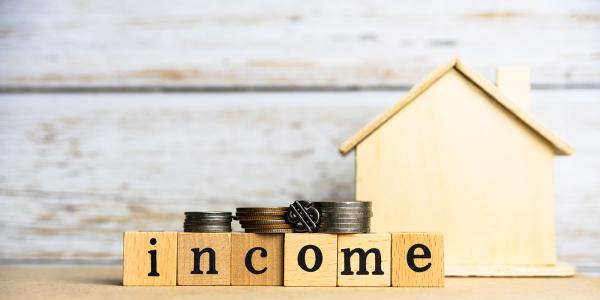 A small wooden house with wooden blocks spelling out the word 'INCOME' on top of the blocks are small piles of coins. A small wooden house with wooden blocks spelling out the word 'INCOME' on top of the blocks are small piles of coins.