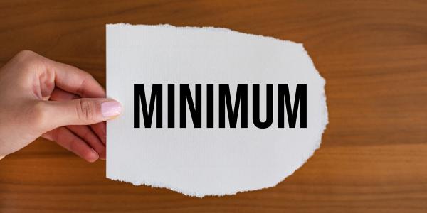 A person holding a piece of white paper with the word 'MINIMUM' typed in black text. A person holding a piece of white paper with the word 'MINIMUM' typed in black text.