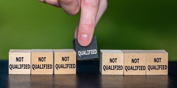 A row of 7 wooden blocks 6 are wooden and have the words 'NOT QUALIFIED' on them, the centre block is black with the word 'QUALIFIED' on it. A row of 7 wooden blocks 6 are wooden and have the words 'NOT QUALIFIED' on them, the centre block is black with the word 'QUALIFIED' on it.
