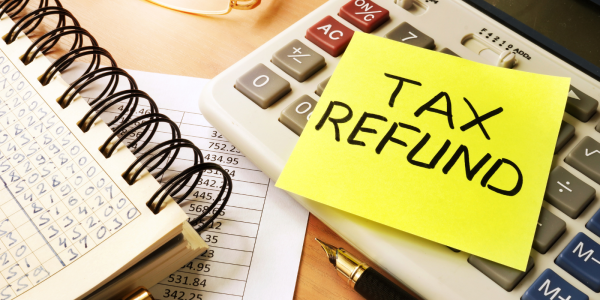 A desk showing various stationary along with a post-it note with the words 'TAX REFUND' written in black ink. A desk showing various stationary along with a post-it note with the words 'TAX REFUND' written in black ink.