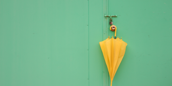 A yellow umbrella hanging on a doorknob against a pale green background. A yellow umbrella hanging on a doorknob against a pale green background.