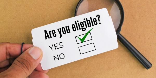 A piece of white card showing the words 'ARE YOU ELIGIBLE?' with tick boxes beneath for 'YES' and 'NO' the tickbox beside the word 'YES' is ticked. A piece of white card showing the words 'ARE YOU ELIGIBLE?' with tick boxes beneath for 'YES' and 'NO' the tickbox beside the word 'YES' is ticked.